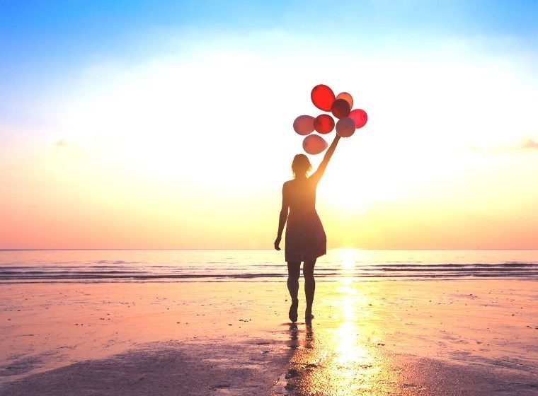 woman holding balloons in sunrise on beach