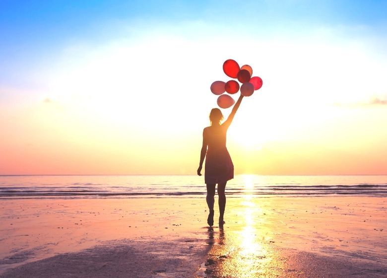 woman holding balloons in sunrise on beach