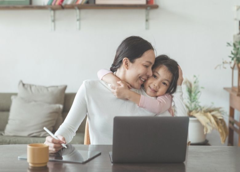Mom loving on child while working from home at laptop